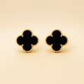 Pair of black clover-shaped earrings with gold outlines on a beige background