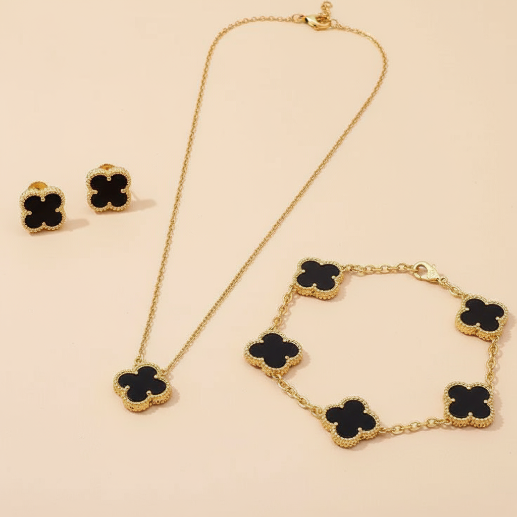 Gold necklace,bracelet and earrings with black clover-shaped pendants on a beige background