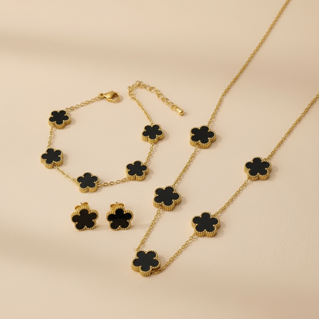 Gold necklace,bracelet and earrings with black flower-shaped pendants on a beige background
