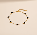 Gold bracelet with black heart-shaped charms on a beige background