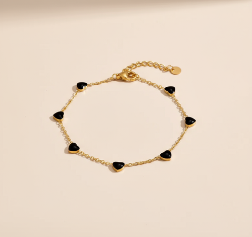 Gold bracelet with black heart-shaped charms on a beige background
