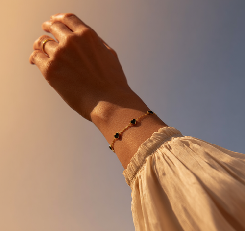 Hand wearing a Black Heart Charm Bracelet with a blurred background