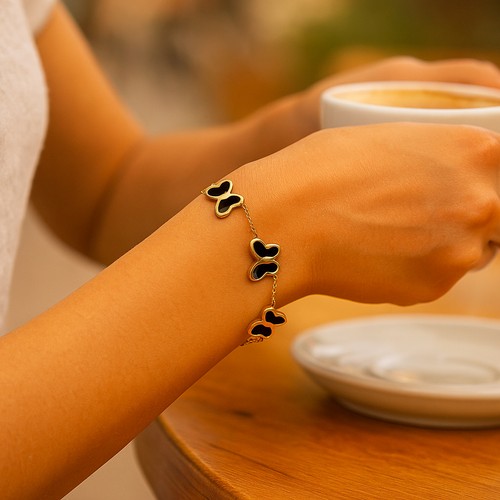 Person holding a cup of coffee with a butterfly bracelet on a wooden table