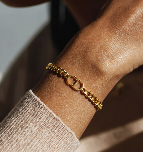 Gold bracelet with 'CD' initials on a wrist against a neutral background