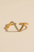Gold ring with wavy design and embedded stones on a beige background