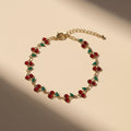 Gold bracelet with red and green beads on a beige background