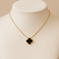 Gold necklace with a black clover pendant on a mannequin bust.