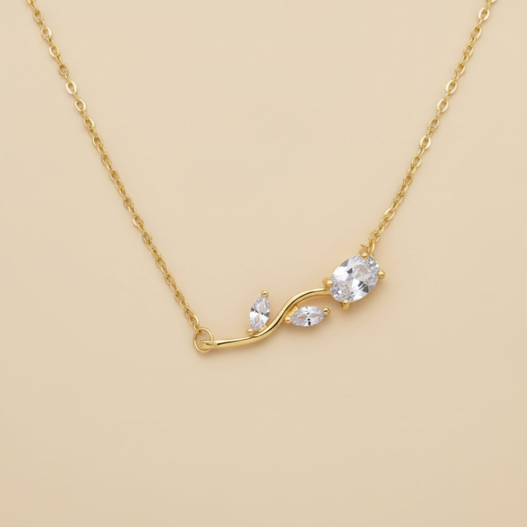 Gold necklace with a leaf-shaped pendant on a beige background