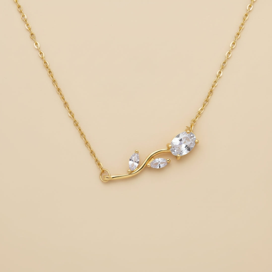 Gold necklace with a leaf-shaped pendant on a beige background
