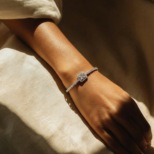 Close-up of a hand wearing a diamond bracelet on a soft beige fabric background
