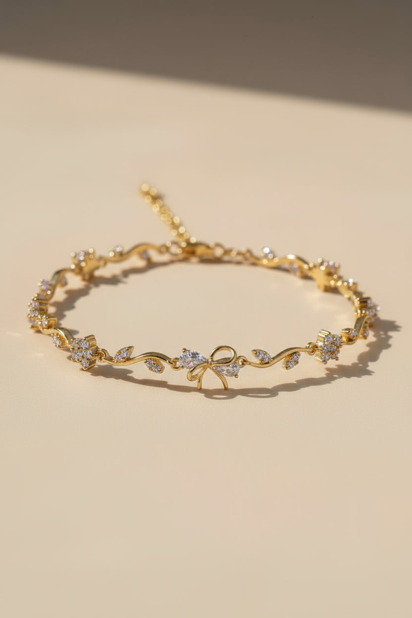 Gold bracelet with floral and bow design on a beige background