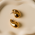 Gold earrings on a beige surface