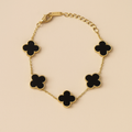 Gold bracelet with black clover-shaped charms on a beige background