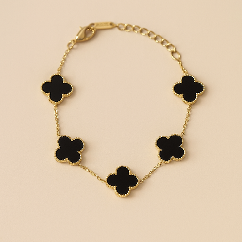 Gold bracelet with black clover-shaped charms on a beige background