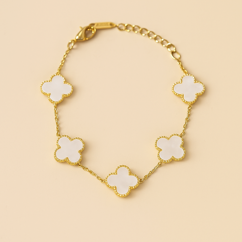Gold bracelet with white clover-shaped charms on a beige background