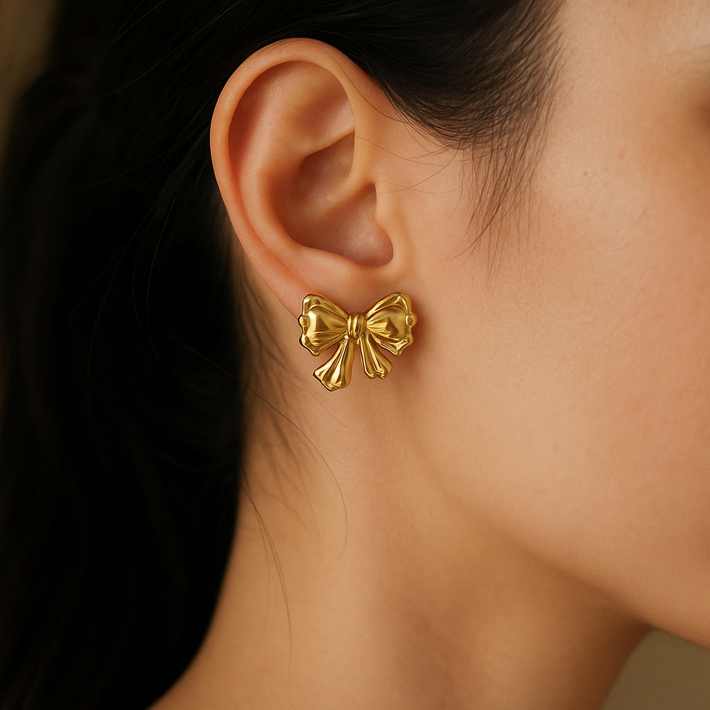 Golden bow-shaped earrings worn by a person with a blurred background