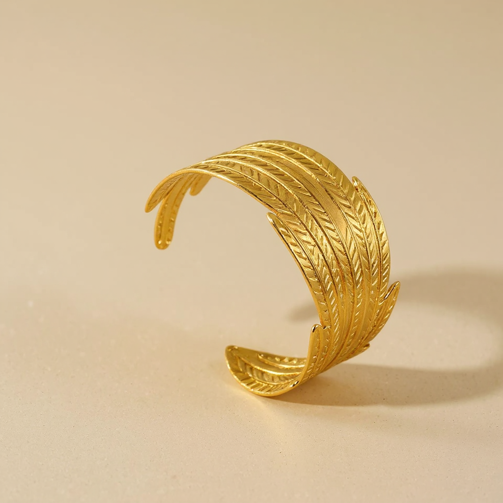 Golden Feather Bangle with leaf-like design on a beige background