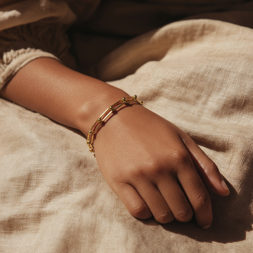 Hand wearing a gold bracelet on a textured beige fabric background