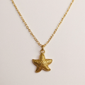 Gold starfish pendant necklace on a light gray background
