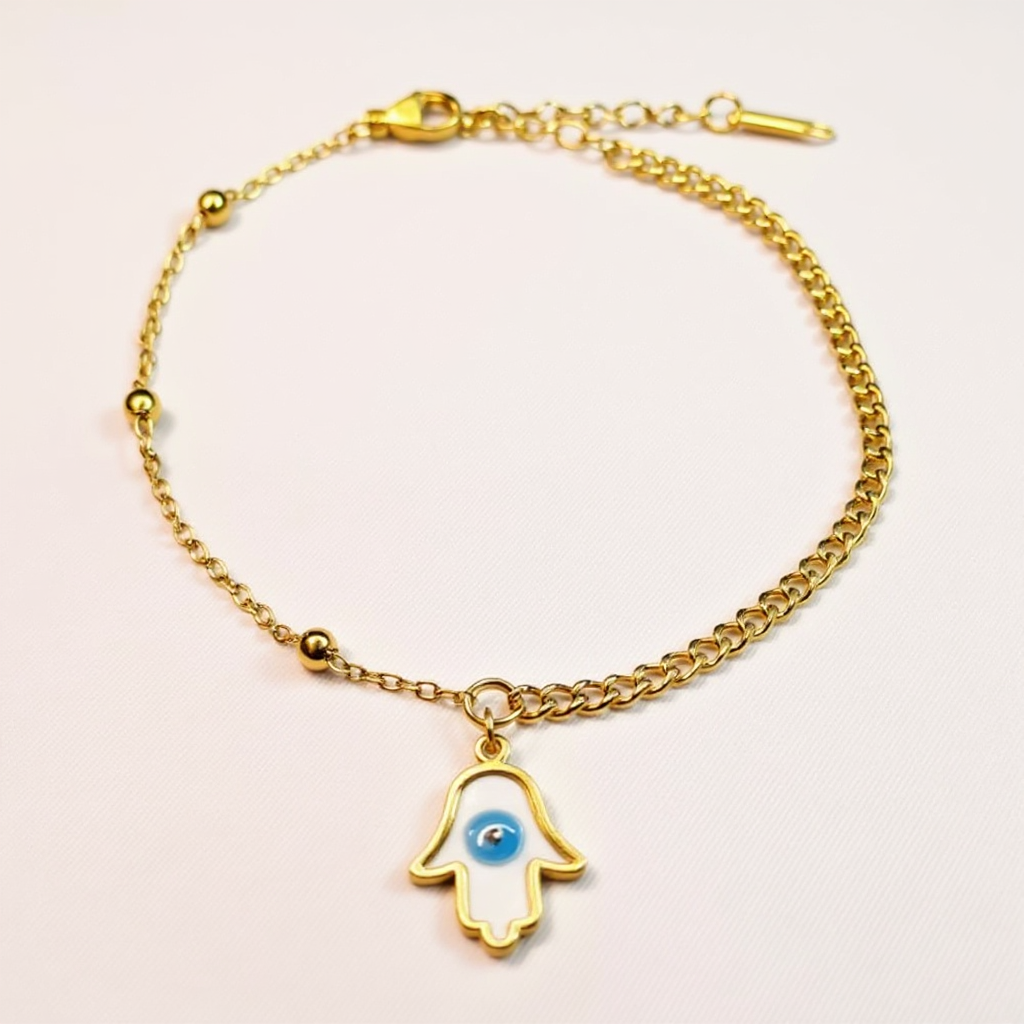 Gold Anklet with a hamsa hand charm featuring a blue eye on a light pink background