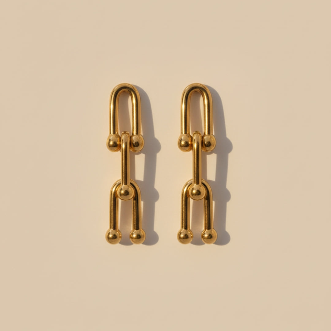Gold chain-style earrings on a beige background