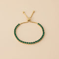 Gold bracelet with green gemstones on a beige background