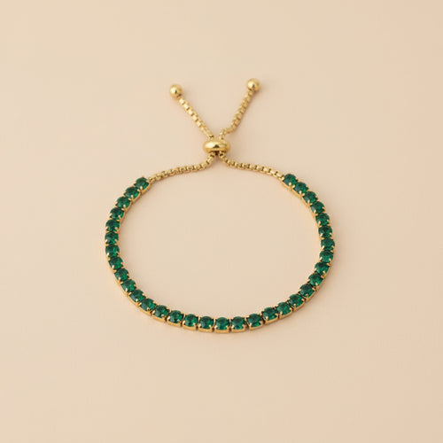 Gold bracelet with green gemstones on a beige background