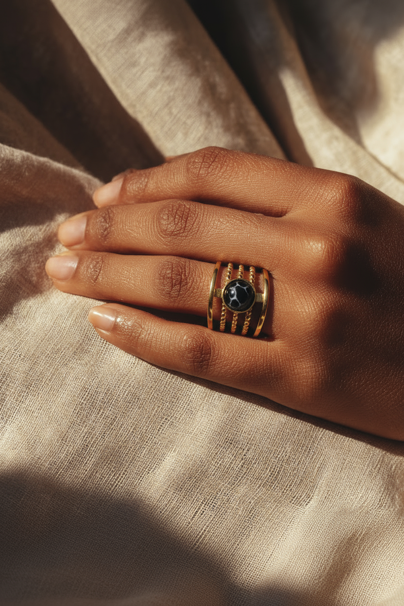 Hand wearing a gold ring with a dark stone on beige fabric