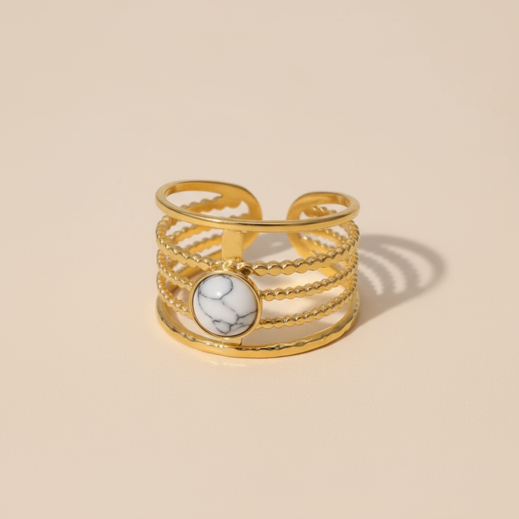 Gold ring with a marble stone on a beige background