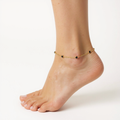 Gold anklet with black beads on a foot against a white background