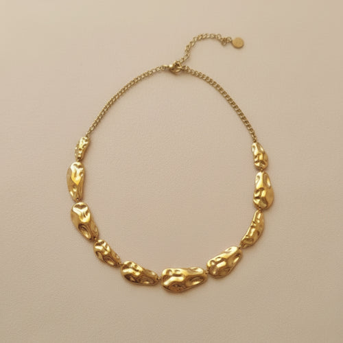 Gold necklace with unique links on a beige background