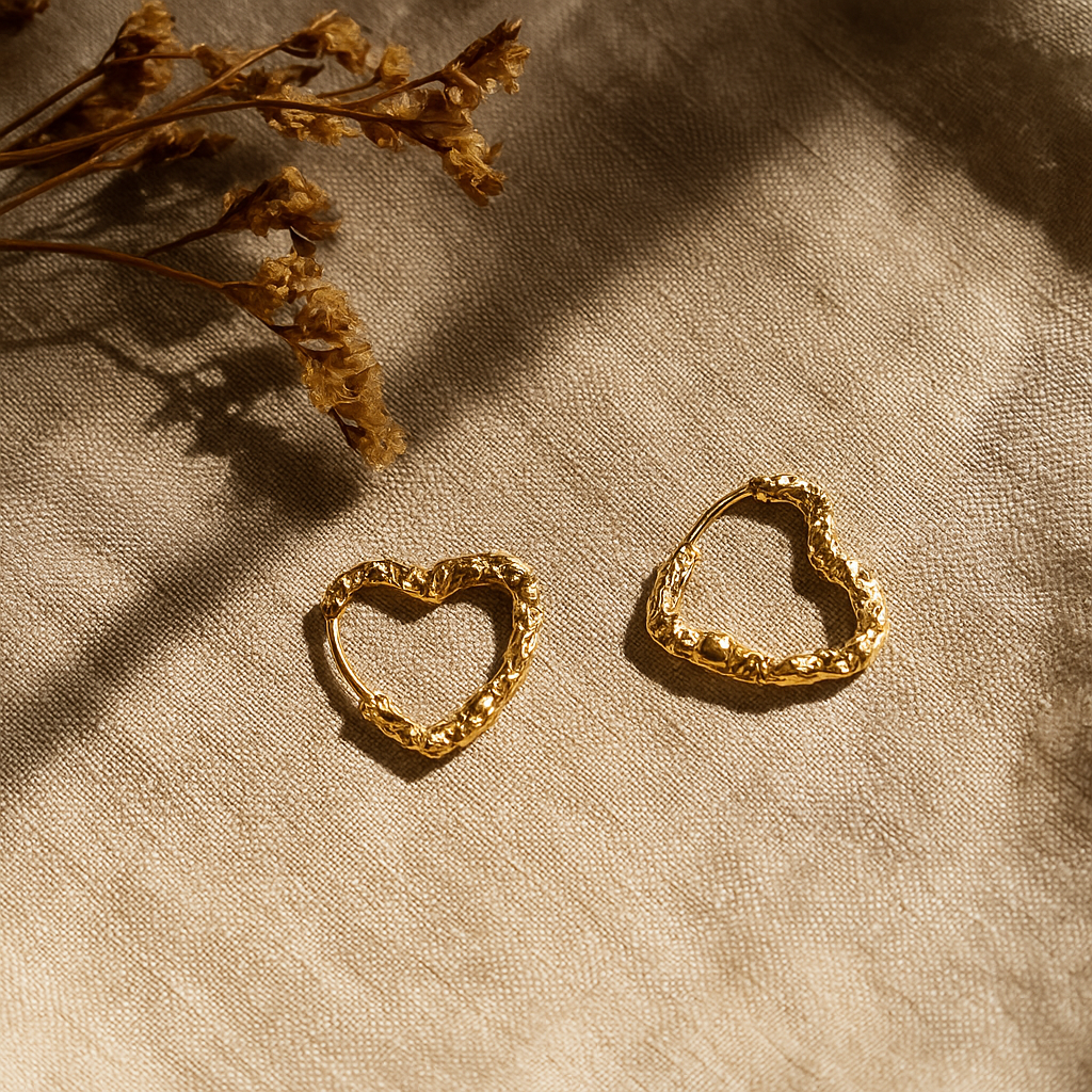 Gold heart-shaped earrings on a textured beige surface with dried flowers.