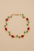 Gold bracelet with red and green gemstones on a beige background