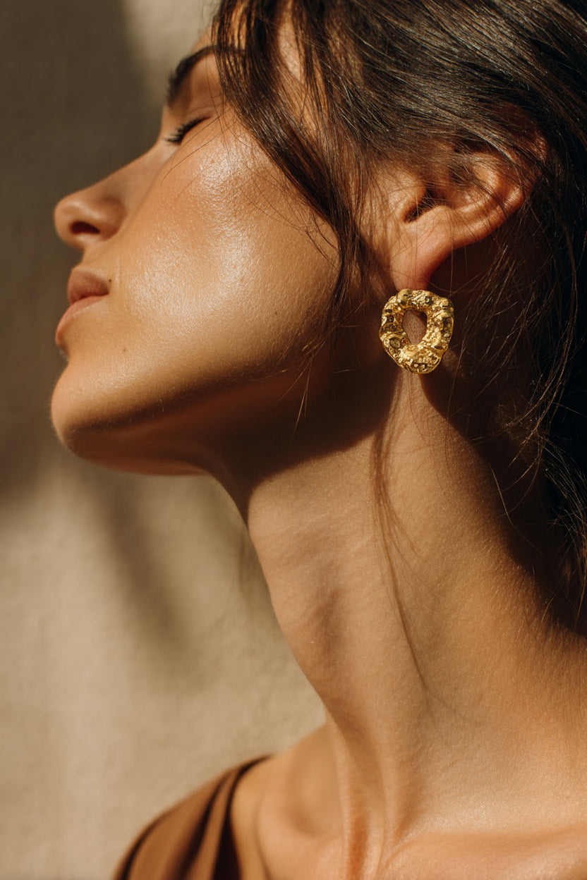 Close-up of a woman wearing gold earrings with a neutral background