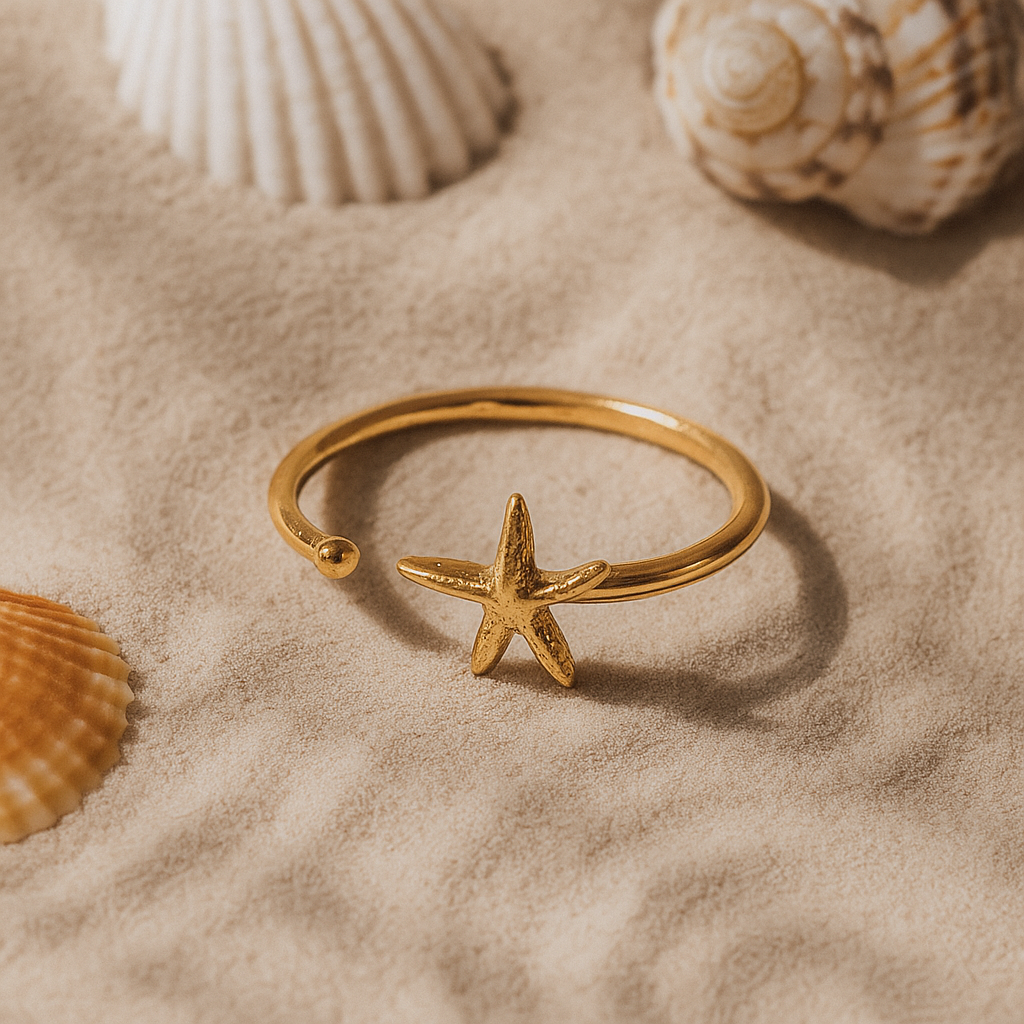 Gold ring with a starfish design on a sandy background with seashells.