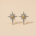 Star-shaped earrings with gold and silver details on a beige background