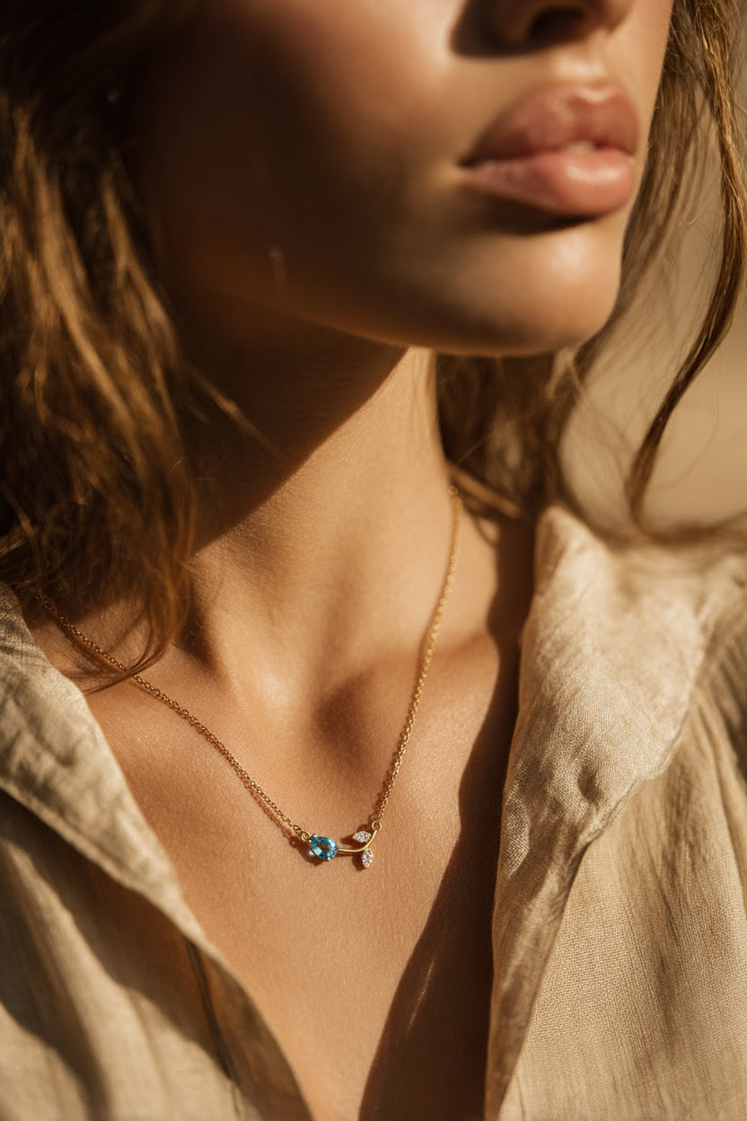 Close-up of a person wearing a necklace with a blue pendant, set against a neutral background.