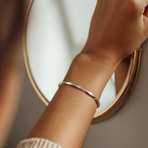 Person holding a black mug with a warm beverage, wearing a silver bracelet, in a blurred indoor setting.