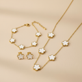 Gold necklace,bracelet and earrings with White flower-shaped pendants on a beige background