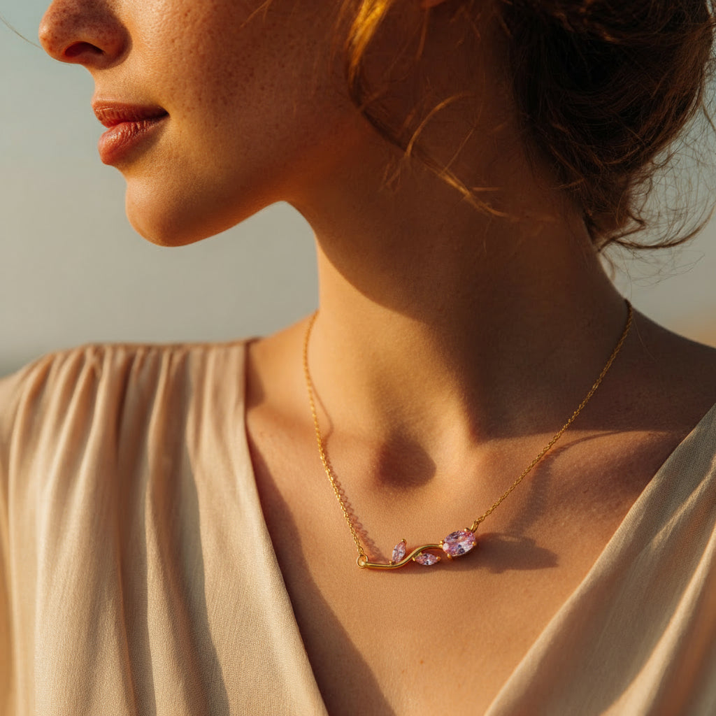 Close-up of a woman wearing a gold necklace with a soft rose gemstones against a neutral background