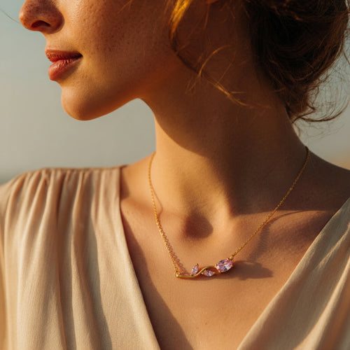 Close-up of a woman wearing a gold necklace with a soft rose gemstones against a neutral background